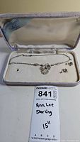 Necklace and two small charms placed inside a jewelry box with cream-colored lining, with the lot label showing brand and length.