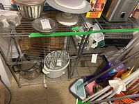Two chrome metal wire shelving units with kitchen-related items displayed on them. Shelving has grid wire shelves and vertical support poles. White floating shelf is visible on top.