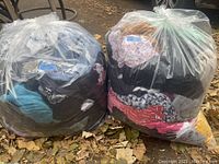 Two large clear plastic bags filled with mixed men's and women's clothing, sealed with a sticker.