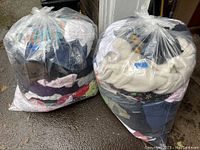 Two large transparent plastic bags filled with assorted his and hers clothing packed and tied at the top.