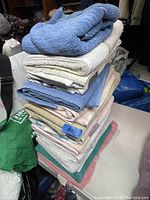 Stack of 12 assorted towels including blue, white, beige, green and pink colors, folded and stacked on a surface indoors.