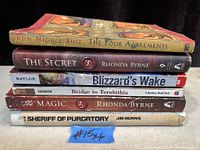 Six books stacked horizontally showing spines with titles and authors, condition visible