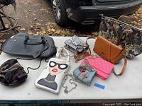 All 8 purses arranged on table outdoors, shows size, style variation, and colors available
