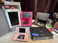 Lot of electronics showing Literati e-reader, pink Nintendo DS, two portable DVD players.