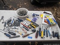 Full view of the assorted hand tools on table including wrenches, pliers, screwdrivers, utility knives, and other small tools.