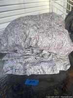 Folded queen bed sheet set showing floral patterns of gray outlined flowers on white fabric.