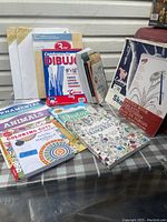 Set of adult and kids coloring books including detailed adult patterns and cute animals, spiral sketch books, and a sketch pad alongside three wooden art panels.