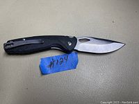 Open folding knife showing the blade and handle details with visible worn blue tape numbered 124