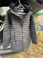 Front view of black Columbia puffer jacket with quilting and attached hood displayed on hanger inside vehicle.