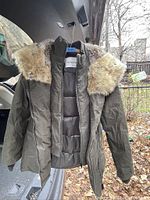Front and open view of an olive green winter jacket parka with puffed sections inside, zipper front, and a hood with a light brown faux fur trim.