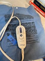 Photo showing the blue SoftHeat electric heating pad with a white control unit connected via a power cord. The control has a sliding switch and heat level indicators.