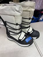 Full side view of two white winter boots with black rubber soles and black adjustable lacing cord, size 6 tag visible