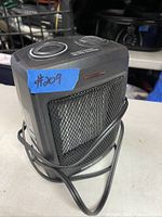 Black compact electric space heater with mesh front and power cord on table.