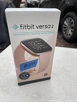Front view of the sealed Fitbit Versa 2 box showing the watch with rose gold-colored case and pink band.