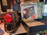 Photo showing the vintage Alltrade 3 in One air compressor and its original box on a table, highlighting the red hazard light and carrying handle on the unit.