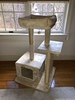 Full view of the cat play house showing the base cubed enclosure, two vertical posts, middle platform and cushioned top perch with raised edges near window