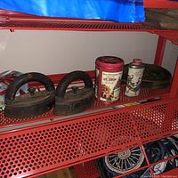 Wide shot showing two cast iron irons and three vintage collectible tins on a red perforated metal shelf.