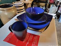 Photo of the dinnerware pieces arranged with mugs, plates, and bowls showing blue inside and matte black outside colors
