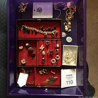 Full view of jewelry tray showing various items including onyx bracelet, pins, and earrings arranged on a purple tray with red velvet inserts.