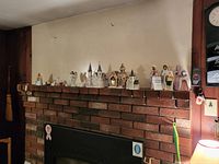 Mantle with the full assortment of ceramic and possibly porcelain nativity figures and several church figurines positioned along the mantle in a row.