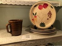 Six fruit motif plates stacked with one displayed on a stand, accompanied by a single brown mug in front.