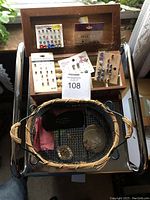 Full lot showing multiple pierced earring sets displayed in a wooden jewelry box with mirror, placed on top of a metal chair. Woven basket below holds other small items.