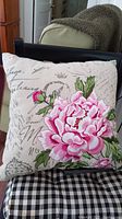 Decorative pillow with pink peony floral design and scripted beige background shown on chair.