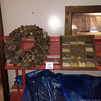 Wide angle of red shelving unit with pinecone wreath hung and wooden tray showing assorted beans arranged in compartments beside it.