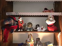 Shelf display of Christmas-themed decorative items including plaid dog toy, golfer figurine, snow globe, cat figure, and Santa stocking with cat face