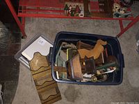 Top view of a plastic container filled with various wooden DIY craft kits and framed pieces, mostly small rocking chairs and wooden plaques