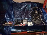 Three items placed on blue tarp: electric train clock and two metal train toys