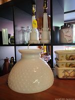 Two tall hobnail milk glass lamps and a hobnail lamp shade, displayed on a shelf