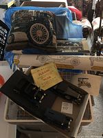 Lot arranged on a table showing pillow with vintage car wheel, small black model car parts, and vintage wallpaper roll with car drawing partially visible.