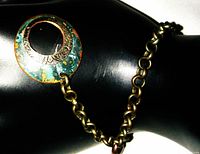 Close-up of handcrafted bracelet showing circular pendant with turquoise patina and linked chain