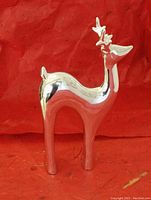 Silver-tone reindeer figurine, approximately 9" tall with smooth reflective finish, standing on a red cloth background