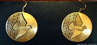 Close-up photo of the pair of intricate gold-toned metal earrings featuring a flying dove and the word "Peace".