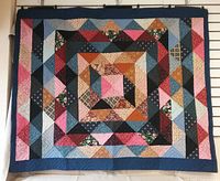 Full view of rectangular patchwork quilt with geometric pattern in multiple fabric colors and prints hung on wall.