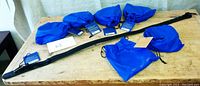 Six black vegan belts laid out with blue branded pouches on a wooden surface. Belts are new and have tags attached.