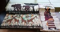 Three rolled pieces of African batik fabric showing animal and human motifs laid out on table.