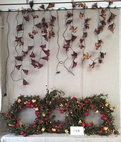 Photo showing two LED floral garlands with hanging brown leaf-like decorations suspended vertically and three floral wreaths laid horizontally below them.