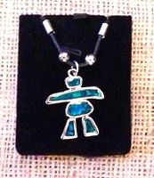 Close-up photo of turquoise Inukshuk necklace on black display pouch, showing silver-tone pendant with turquoise inlay on black cord with silver beads.