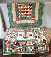 Green-border quilt with heart-shaped chevron patchwork design laid over wooden surface and hanging behind it.
