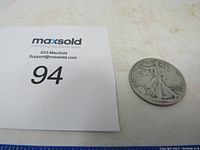 Photo showing the front side of the 1942 Standing Liberty half dollar coin lying flat next to a MaxSold card with number 94.