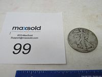 Photo of the 1945 Standing Liberty Half Dollar coin on a white surface with a MaxSold lot number card and ruler for size reference.