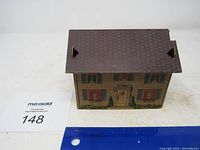 Front and side view of the antique decorative metal house model showing painted siding, shutters, door, and roof details.