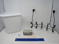 Photo showing Baldwin candle box, white plastic trash can, and black metal wall hanger on white background with blue ruler.