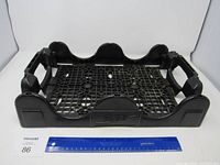 Front view of the black plastic Coca Cola crate showing the lattice bottom and side handles with a ruler for scale.