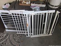 Image showing the child gate laid on the floor with both mounting frames and the main gate with vertical bars, latch, and adjustable mounting hardware visible.
