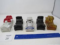 Front view of all five glass decorative car bottles lined up with ruler for scale, colors include red/white, black, clear and amber.