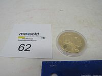 Top-down view of the gold coin replica beside a MaxSold label and a ruler, showing relative size.